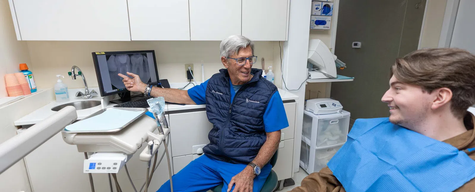 Senior male dentist explaining dental X-ray results to a young male patient in a modern dental clinic.