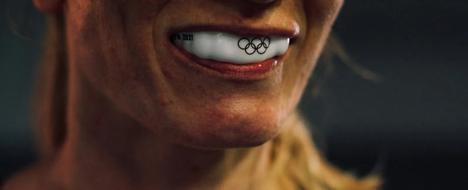Close-up of athlete smiling with white mouthguard featuring Olympic rings logo