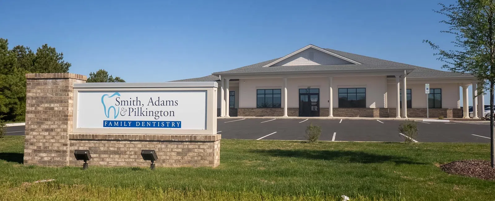 Front view of Smith Adams Pilkington Family Dentistry building and sign under clear blue sky.