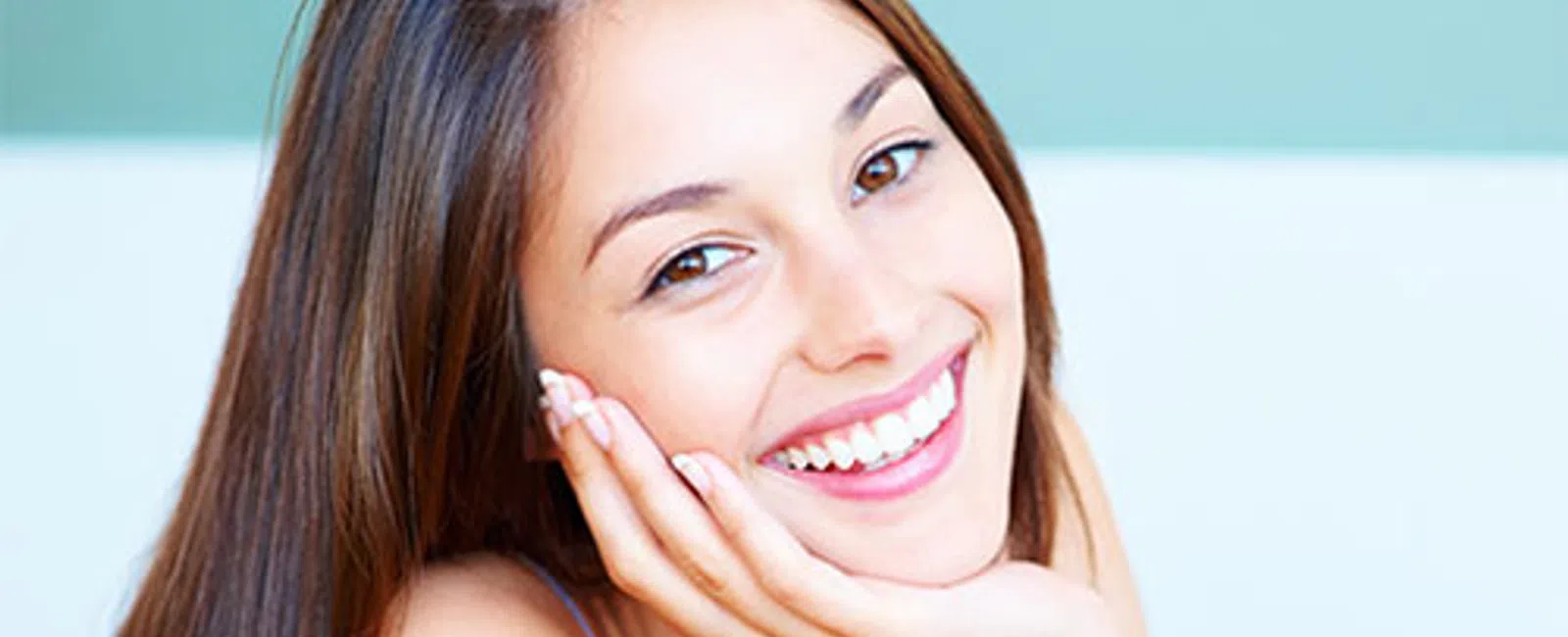 Close-up of a young woman smiling with hand resting on her cheek against a soft blue background
