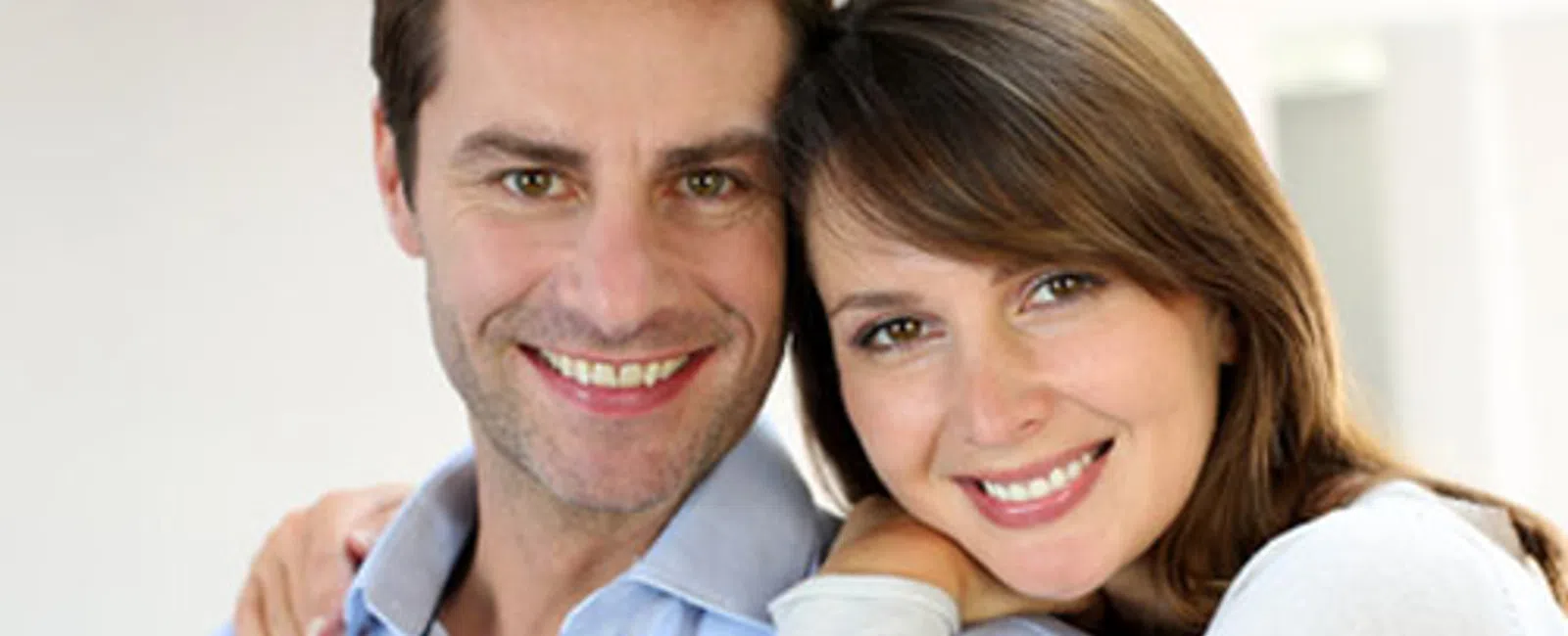 Smiling couple with arms around each other in a bright, cozy indoor setting showing affection and happiness.