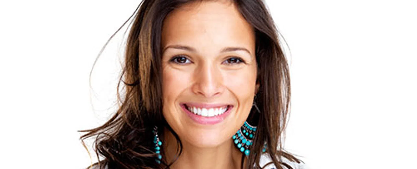 Smiling woman with long brown hair wearing turquoise earrings and a white patterned top against white background
