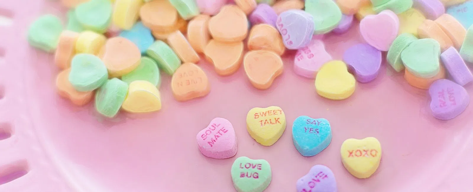 Colorful heart-shaped candy with love messages on a pink plate, perfect for Valentine's Day.