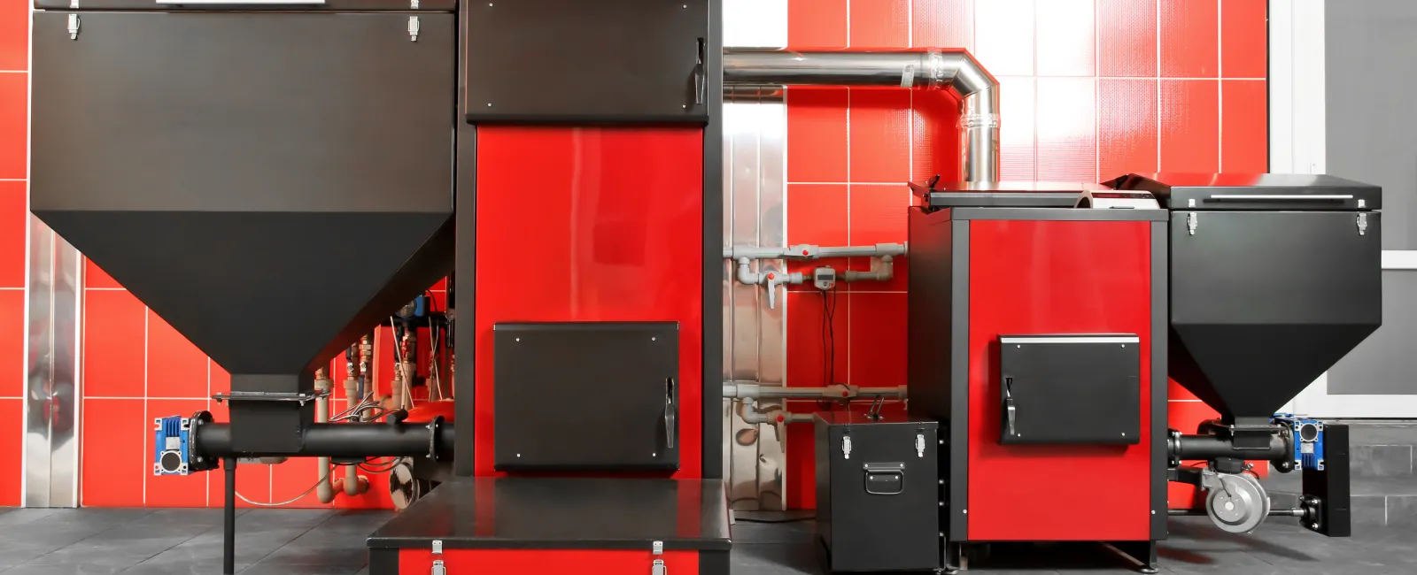 Modern red and black industrial pellet boilers against a red tiled wall in a clean utility room.