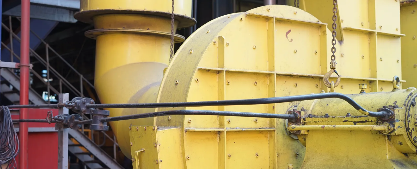 Close-up of large yellow industrial machinery with pipes and metal supports in a factory setting