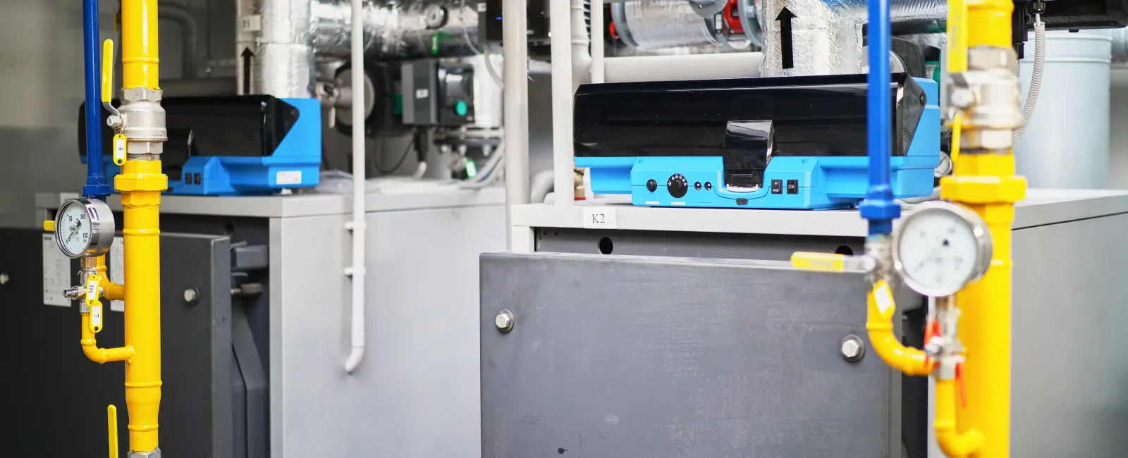 Industrial boiler system with yellow gas pipes, pressure gauges, and blue control units in mechanical room