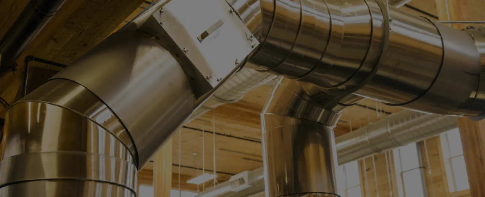 Stainless steel industrial ventilation ducts in a modern wooden ceiling building interior with natural light.