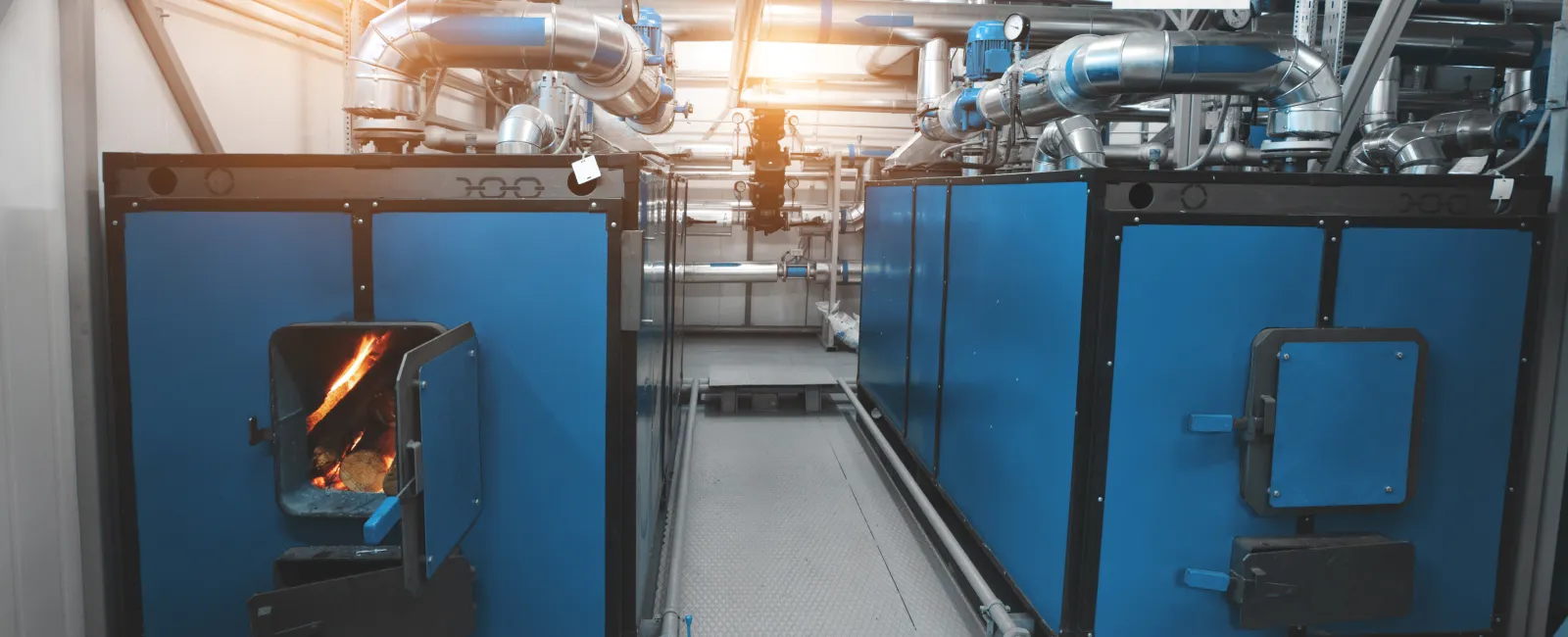 Industrial boilers with blue panels and visible fire inside one unit in a clean mechanical room.