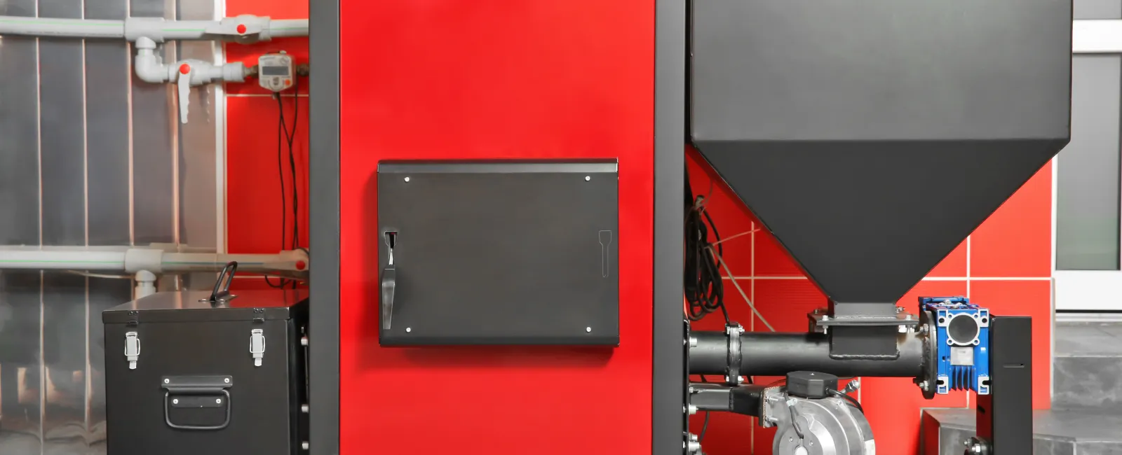 Industrial red and black pellet boiler heating system installed in a tiled room on a gray floor.