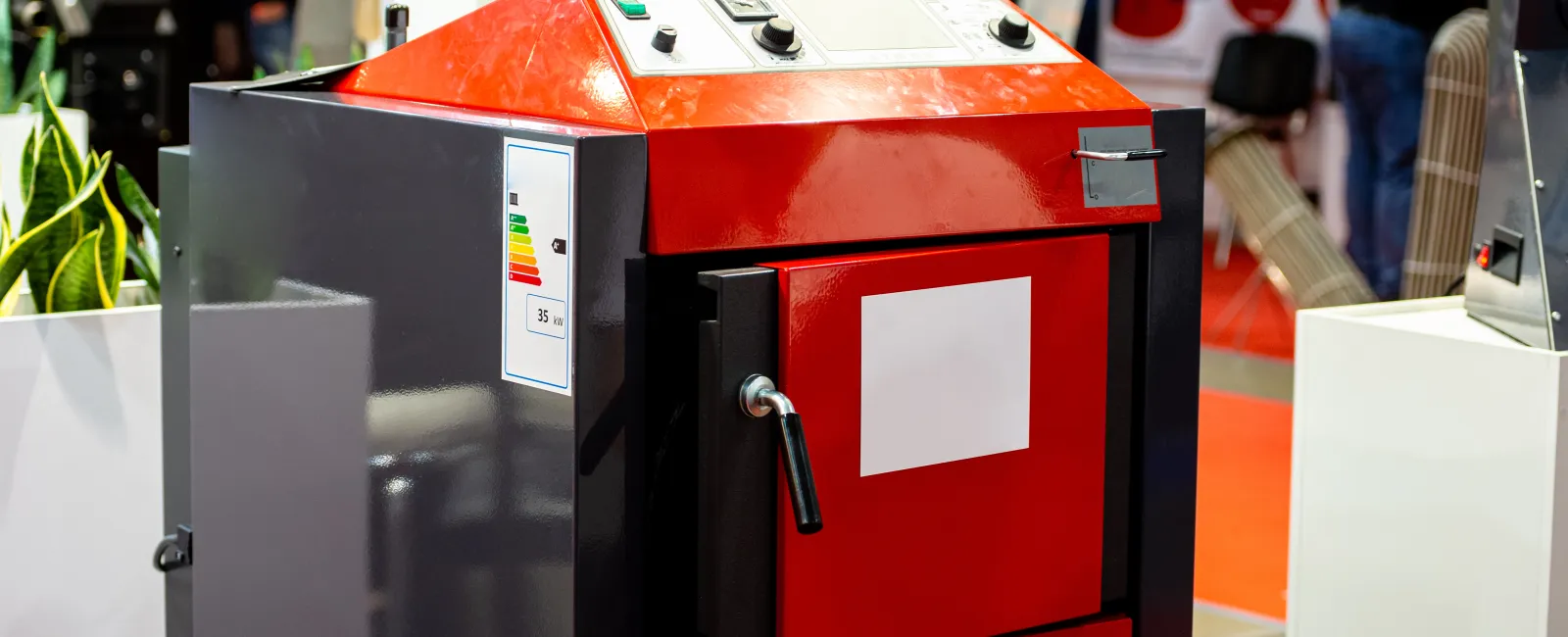 Red and black industrial heating boiler with control panel and door handle on display at trade show