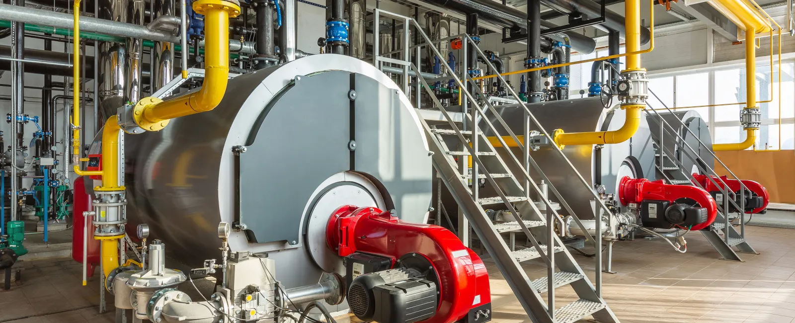Industrial boilers with red burners and yellow pipelines in a factory boiler room.