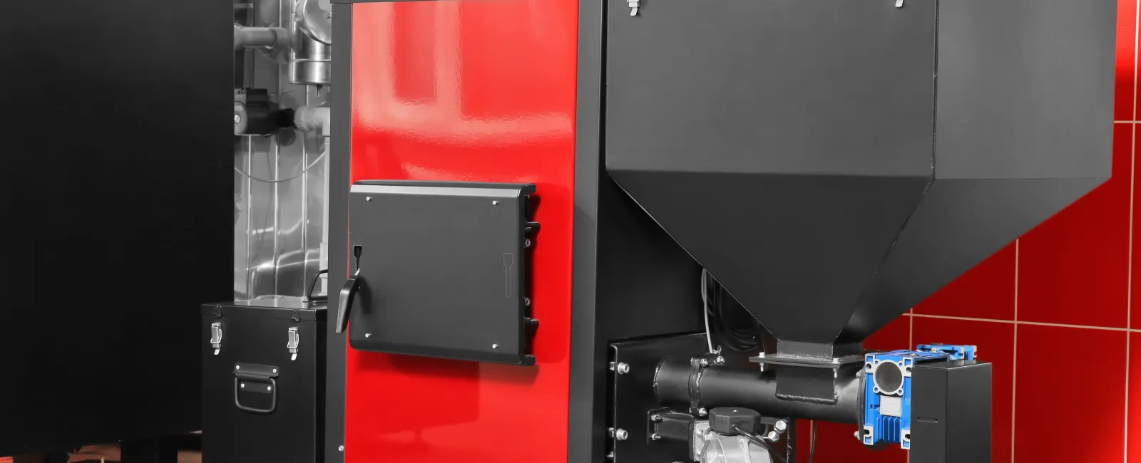 Modern industrial pellet boiler in red and black with attached hopper in a tiled room