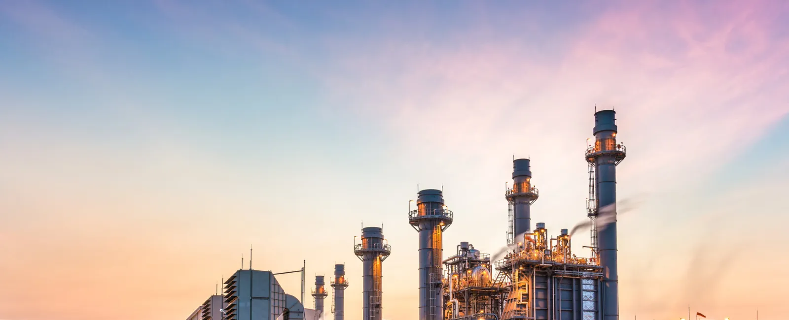Industrial power plant with tall chimneys and complex structures under a colorful twilight sky.