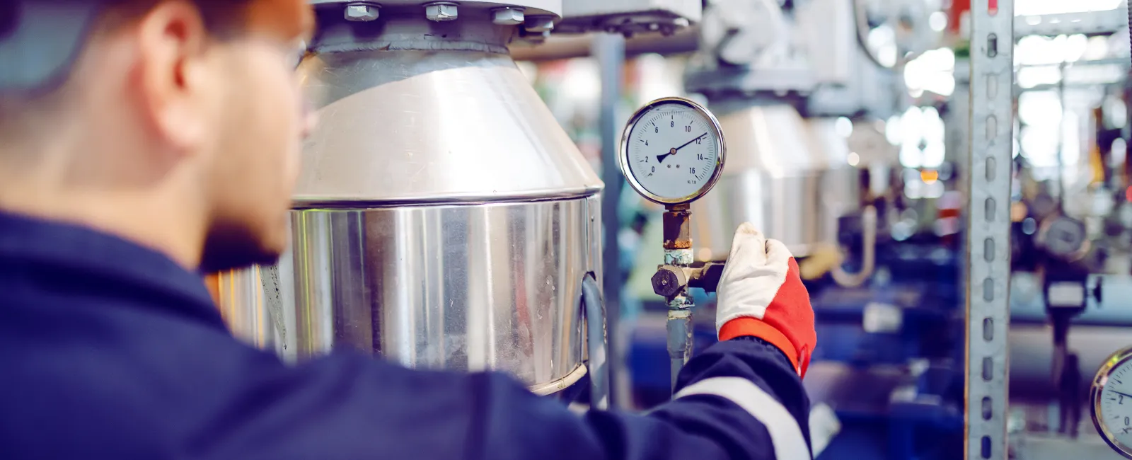 Engineer in yellow helmet checking pressure gauge on industrial machinery in factory setting