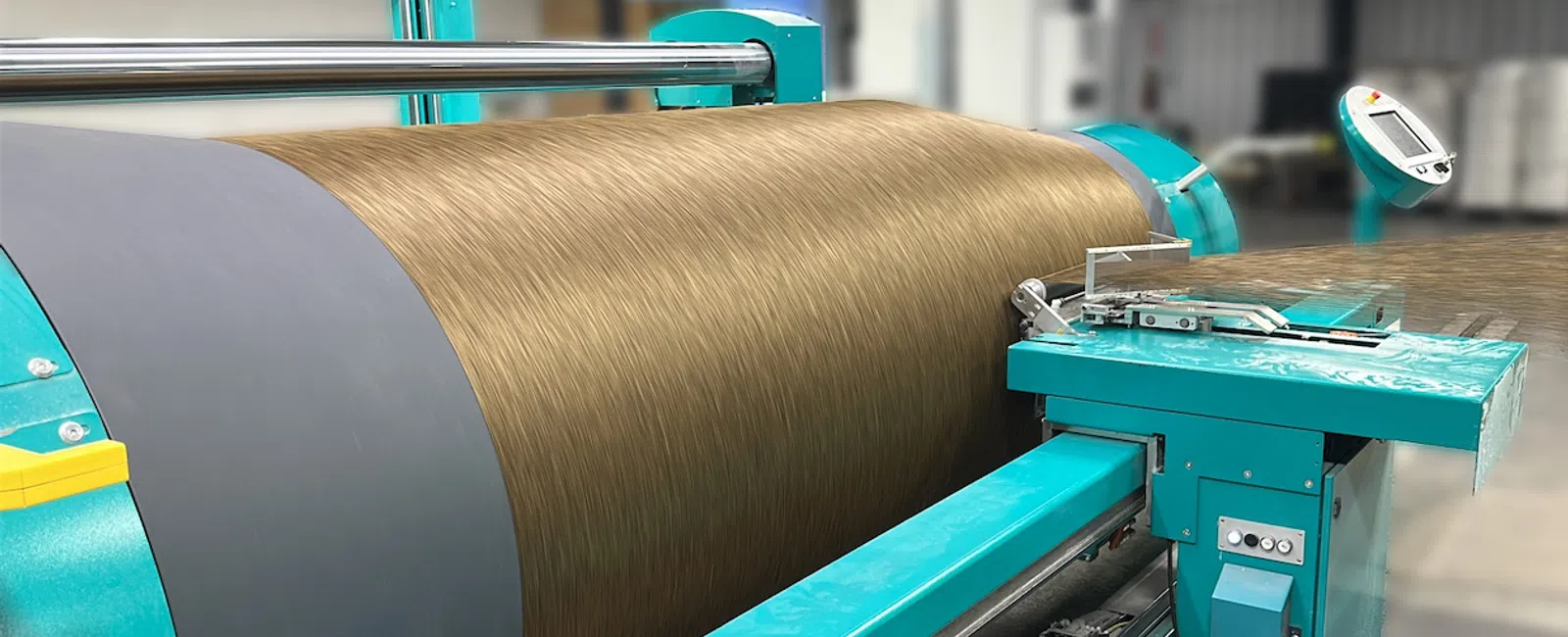 Industrial machine winding brown textile fiber in a factory setting with teal machinery components.
