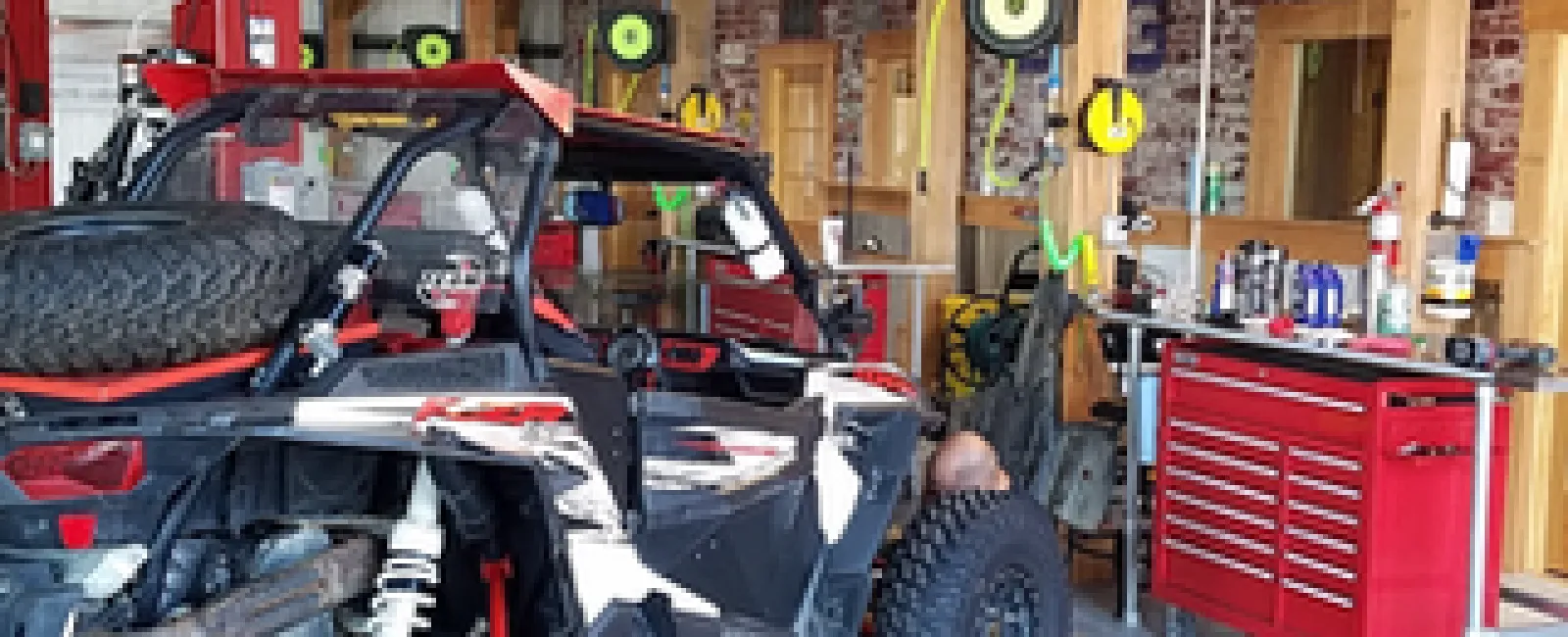 Off-road vehicle with large tires in a garage workshop with red tool chest and wooden beams