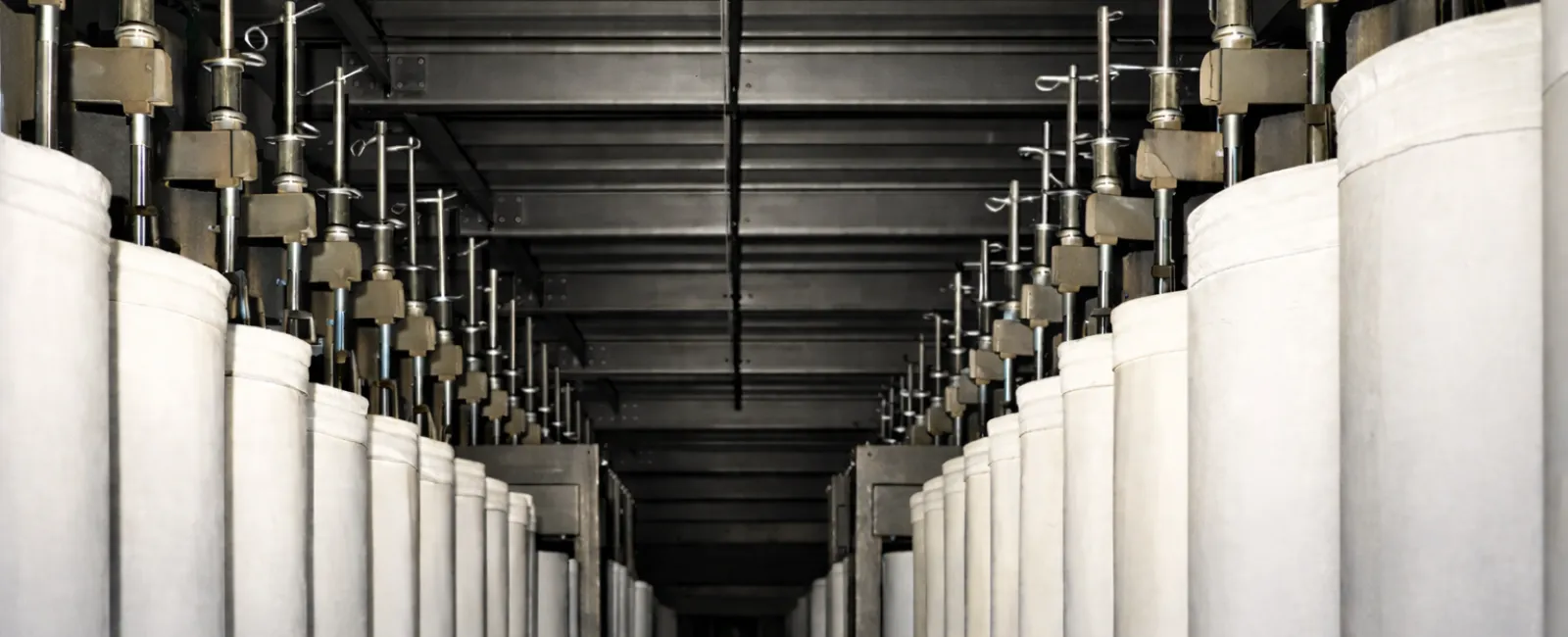 Rows of industrial fabric filter bags hanging in a factory setting with metal supports and ceiling structure.