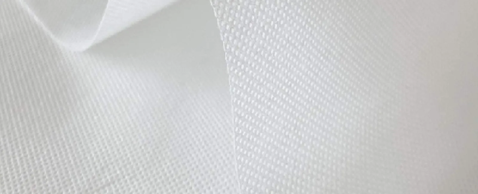Close-up of white textured fabric with visible mesh pattern and soft folds creating depth and shadow.