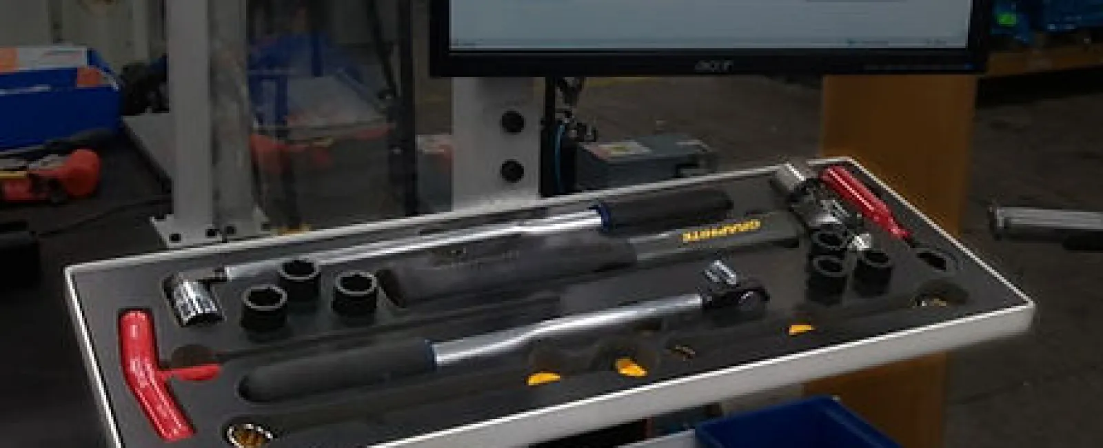Tray of torque wrenches and sockets displayed on a workstation with a computer monitor in the background.