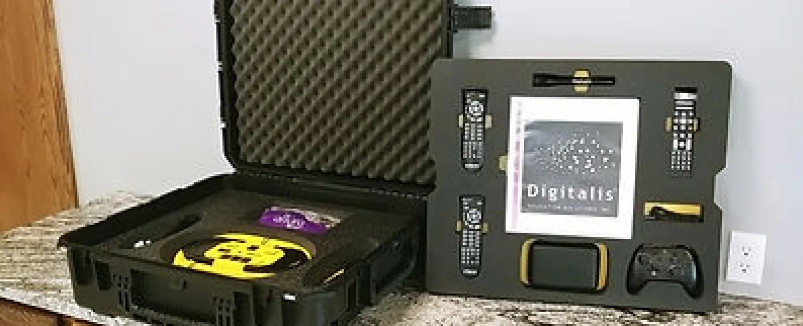 Black hard case with foam padding holding a digital kit including remotes, controllers, and a touchscreen device