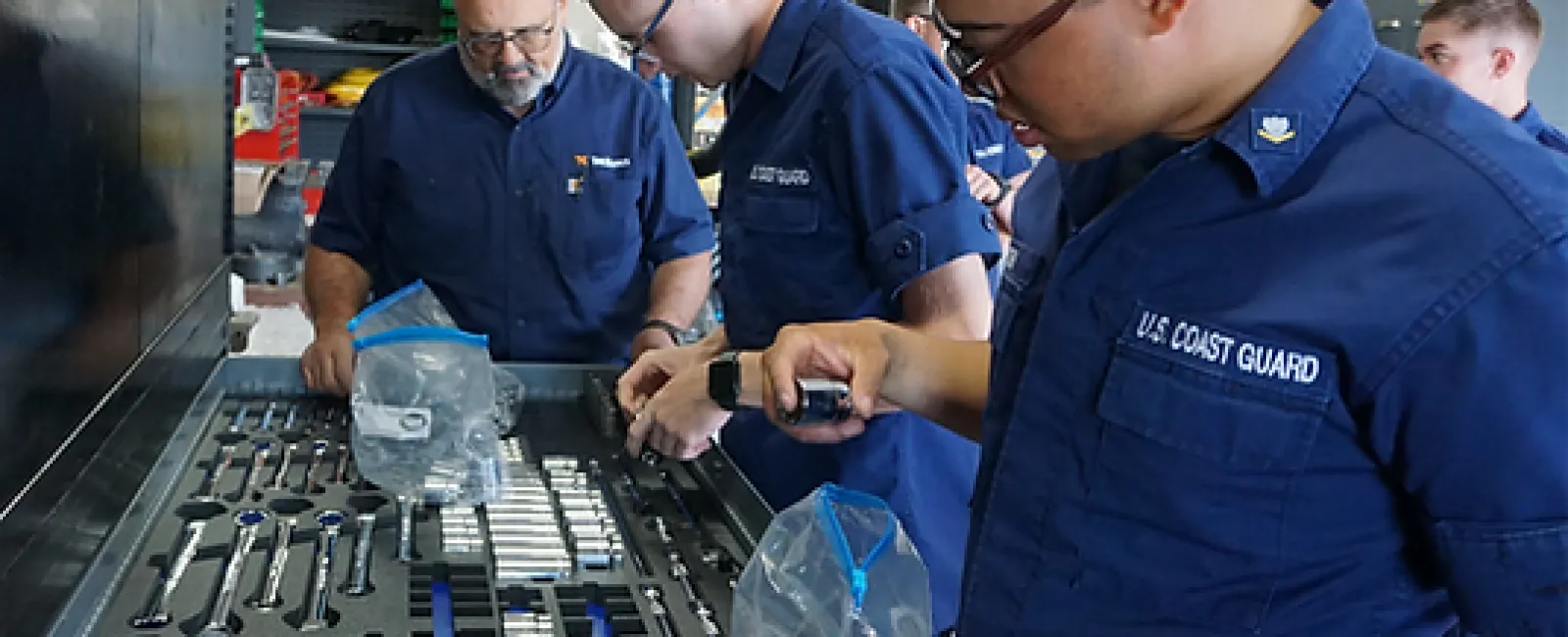 U.S. Coast Guard personnel sorting and organizing tools in a maintenance workshop for equipment readiness