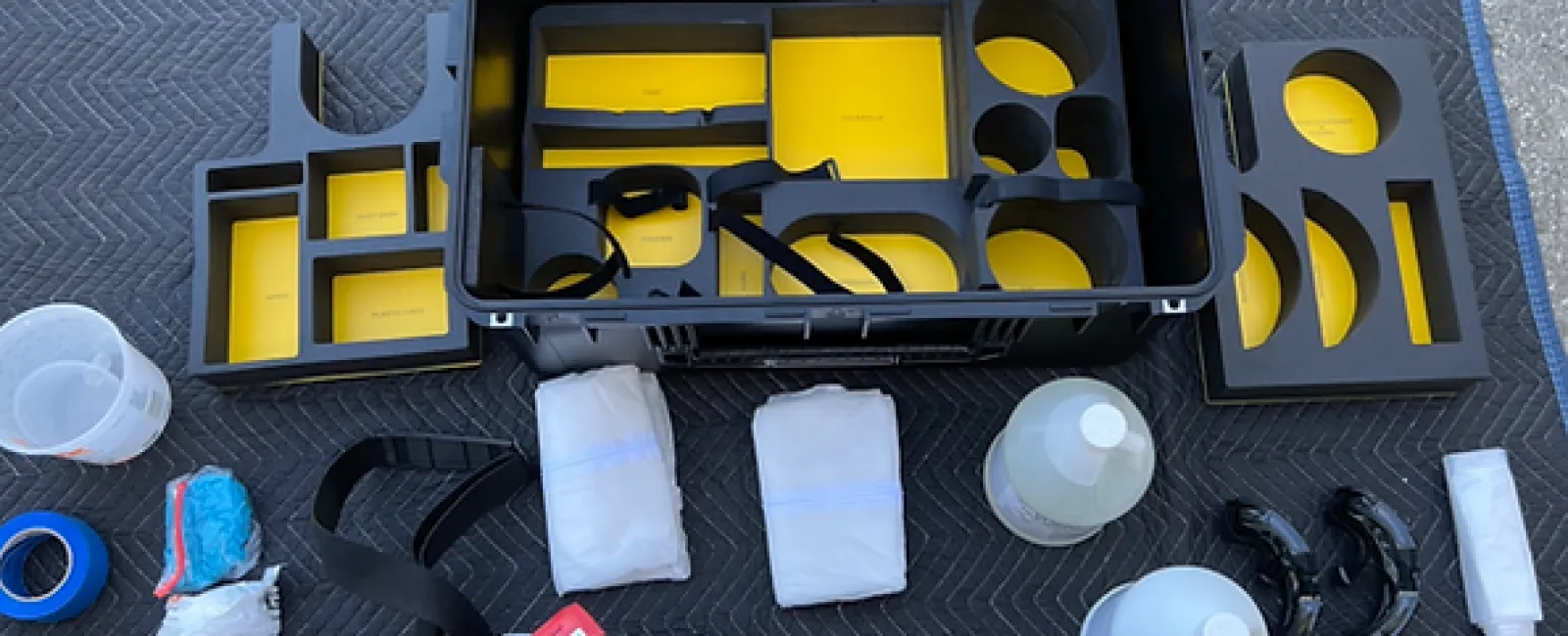 Open black equipment case with yellow inserts surrounded by automotive detailing tools and cleaning supplies on black mat.