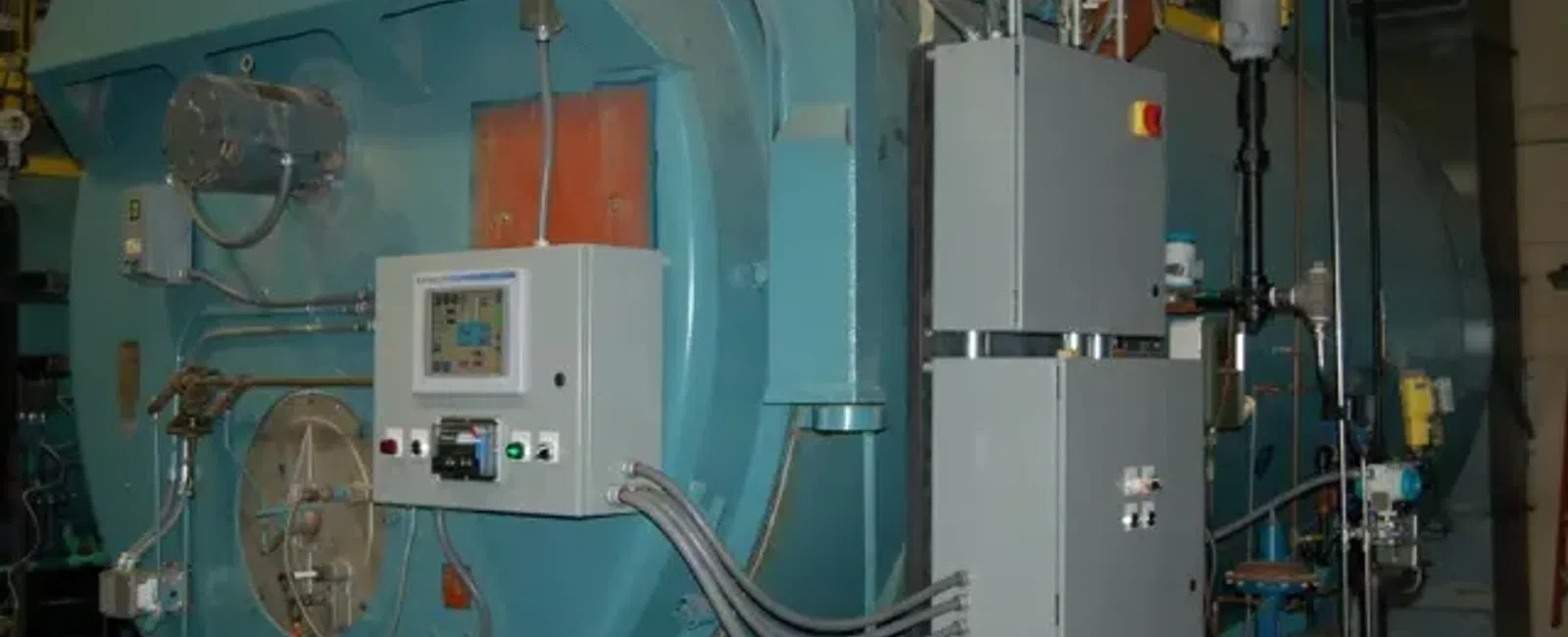 Large blue industrial boiler with control panels, pipes, and gauges in a factory setting.