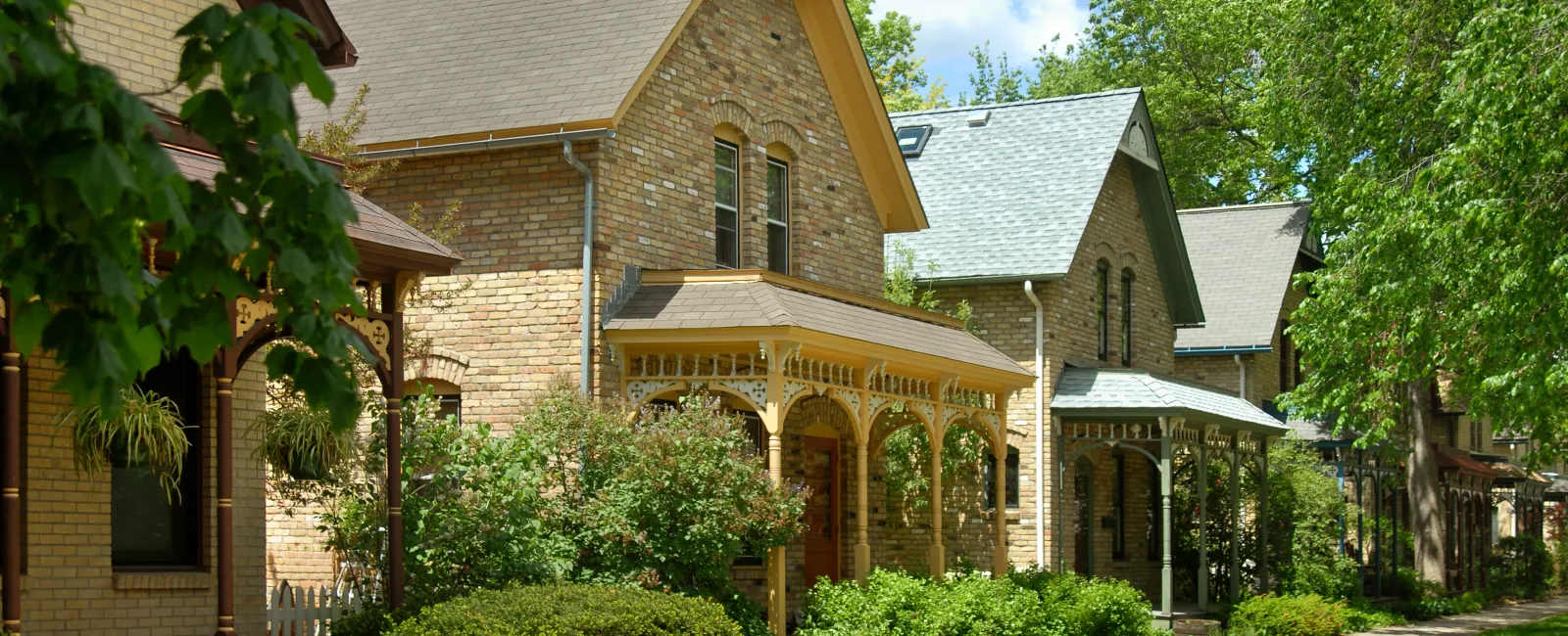 Charming neighborhood featuring traditional brick houses with lush greenery and walkways on a sunny day.