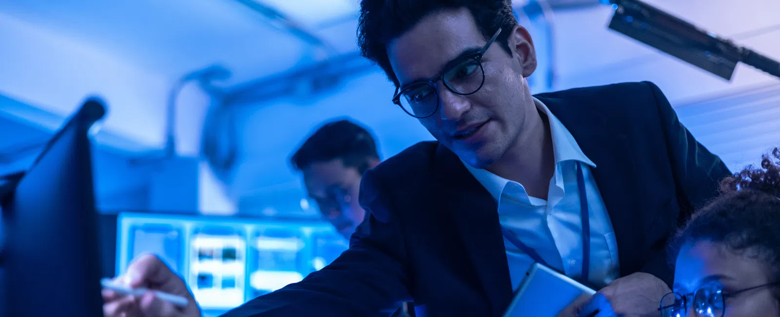 Business team collaborating on data analysis in a modern office with multiple digital screens and blue lighting.