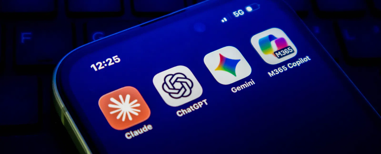 Smartphone screen showing AI app icons Claude, ChatGPT, Gemini, and M365 Copilot on a dark background.