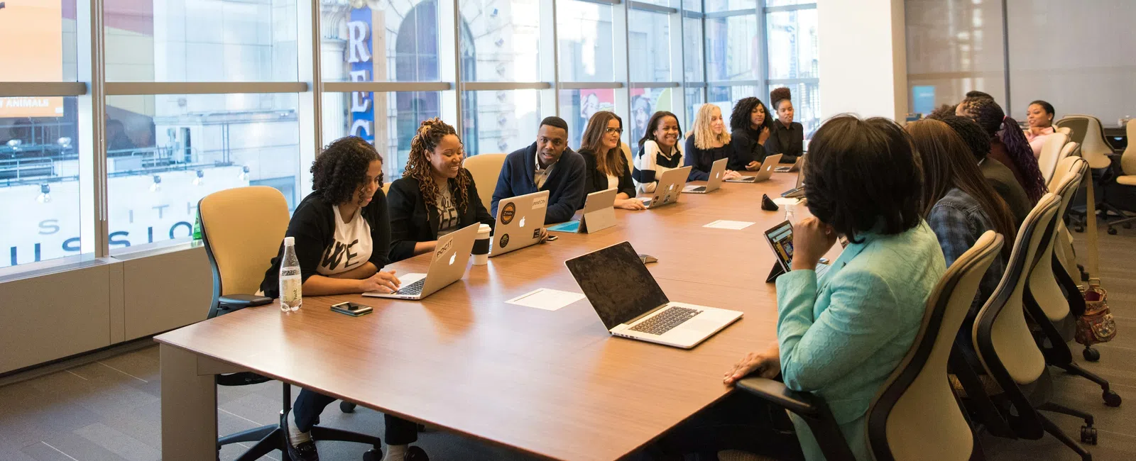 Diverse group of professionals working on laptops around a large conference table in a modern office.