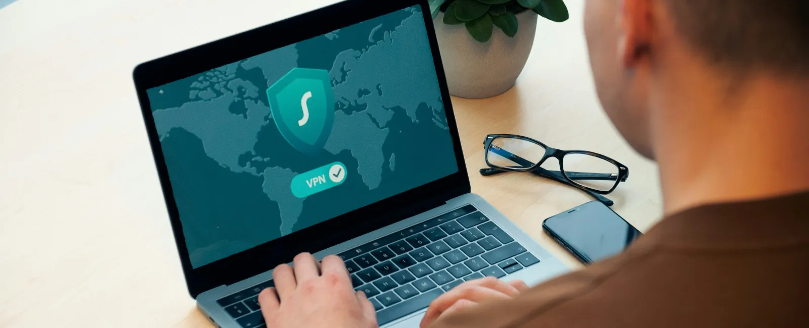 Person using a laptop with VPN enabled showing a secure shield icon on a world map background