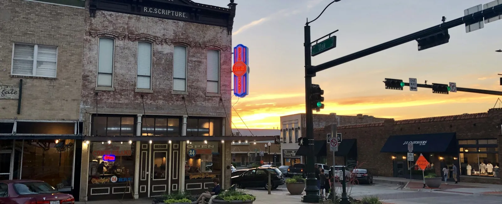 Historic building with R.C. Scripture sign and sunset over downtown street with traffic lights and cars.