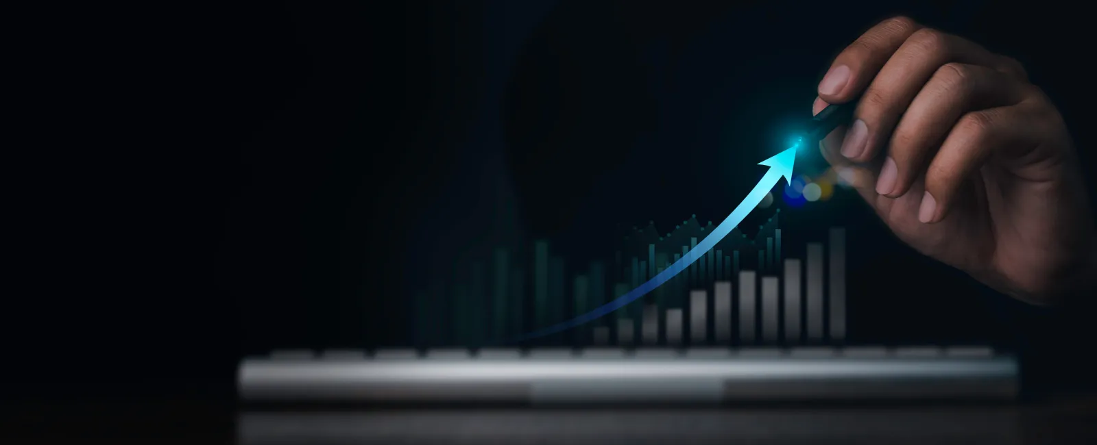 Hand drawing a glowing upward arrow over rising bar chart on dark background above keyboard.