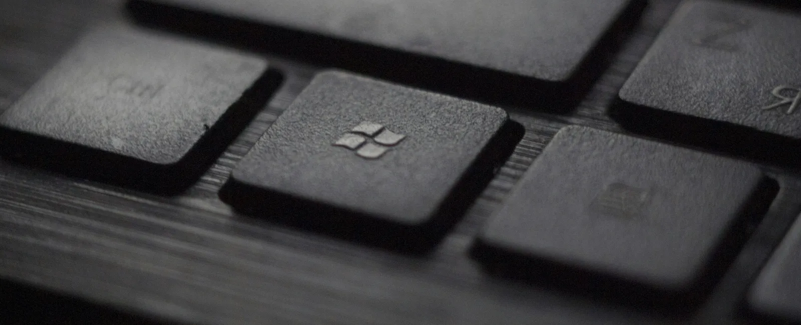 Close-up of a black keyboard with a Windows key in focus on a dark wood surface.