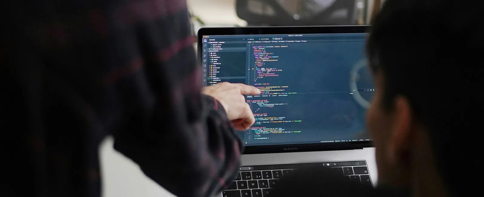 Two people collaborating on coding displayed on a laptop screen in a modern office setting.