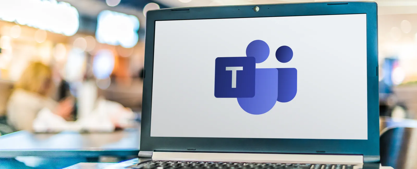 Laptop displaying Microsoft Teams logo on screen in a bright, blurred office environment.