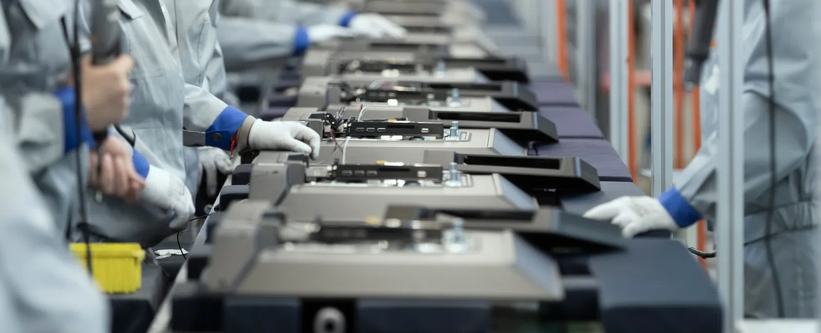 Workers assembling electronic devices on a factory production line wearing protective gloves and uniforms.