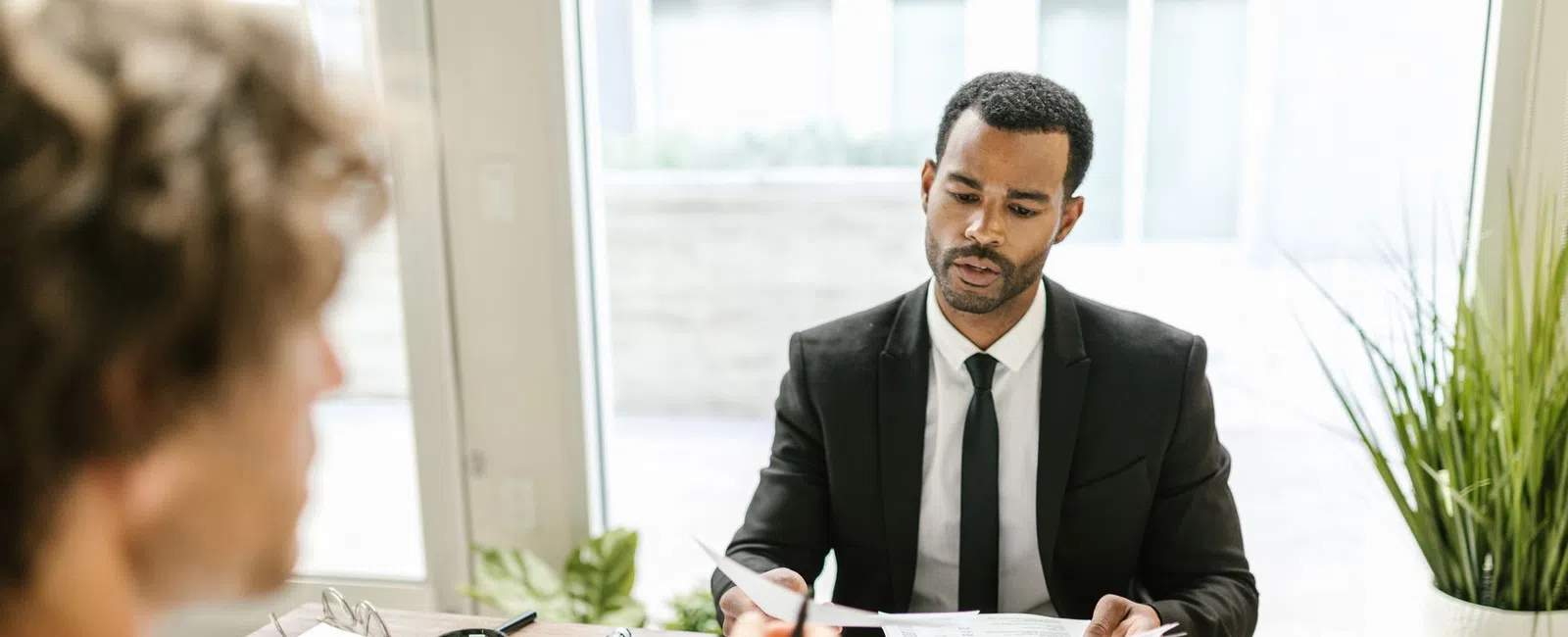 Two professionals discussing documents during a business meeting in a bright office with natural light.