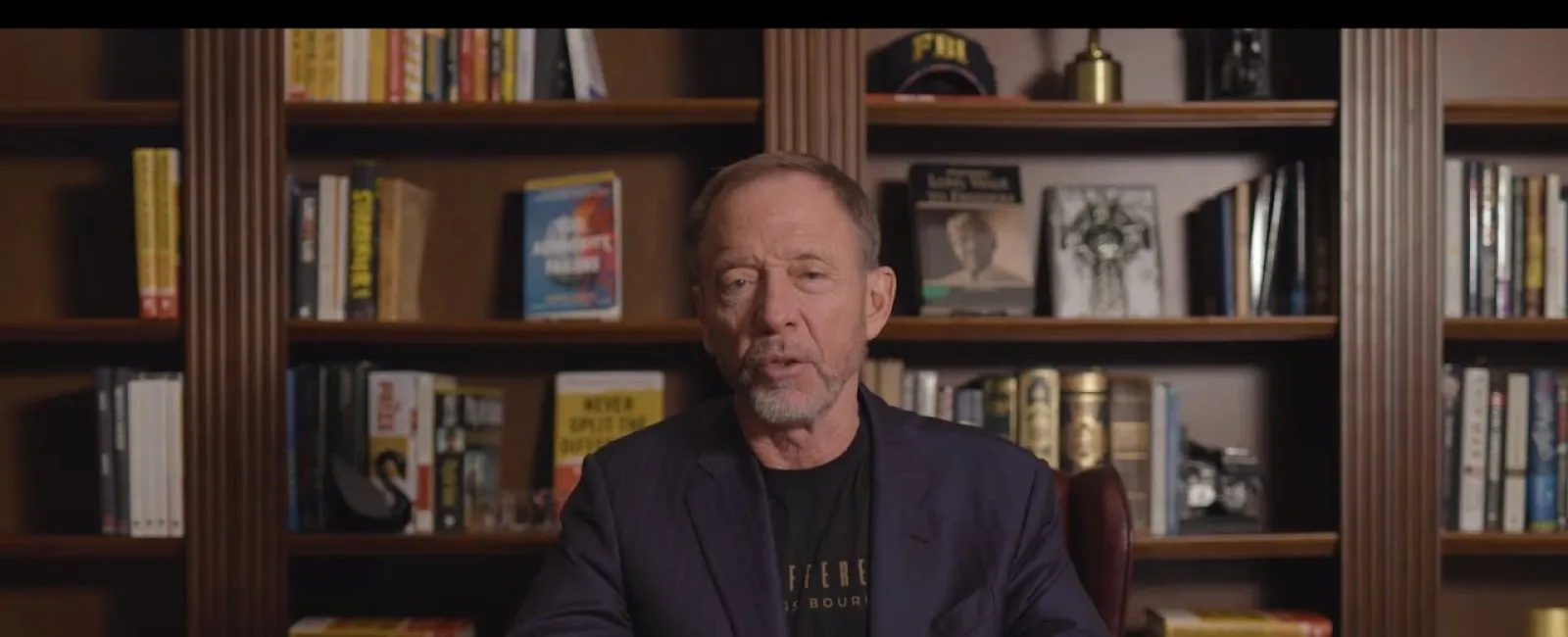 Chris Voss speaking in front of a wooden bookshelf with books and FBI memorabilia, introducing himself as a former FBI negotiator.