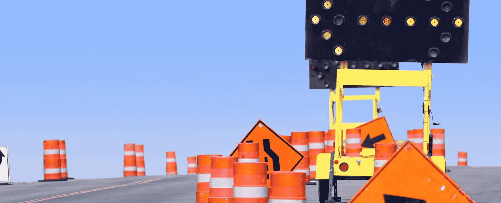 Roadwork zone with orange traffic barrels, directional arrow signs, and electronic arrow board on a clear day.