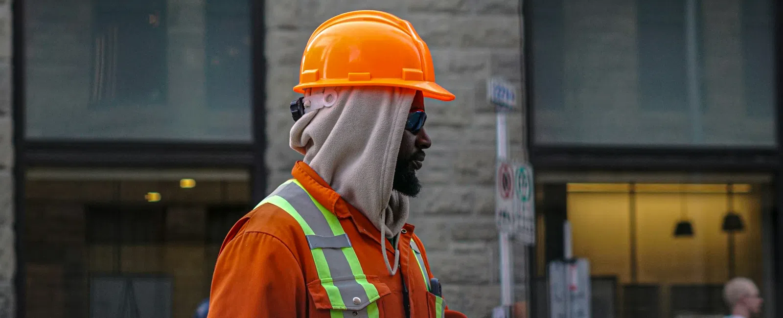 Construction worker in orange safety gear and helmet fist bumping another person on urban street.