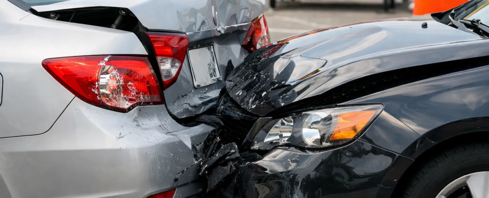 Two cars collide in a rear-end accident at a road work zone with orange cones and warning signs.