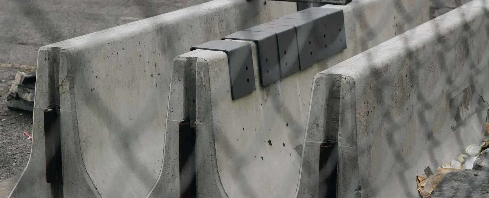 Stacked concrete barriers behind chain-link fence on a construction site with asphalt ground