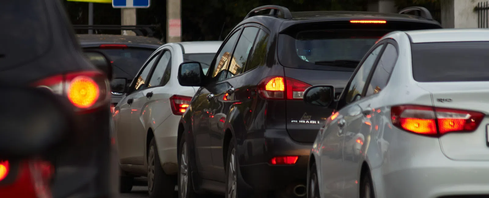 Multiple cars lined up in traffic on a city street with brake lights illuminated and traffic signs visible.