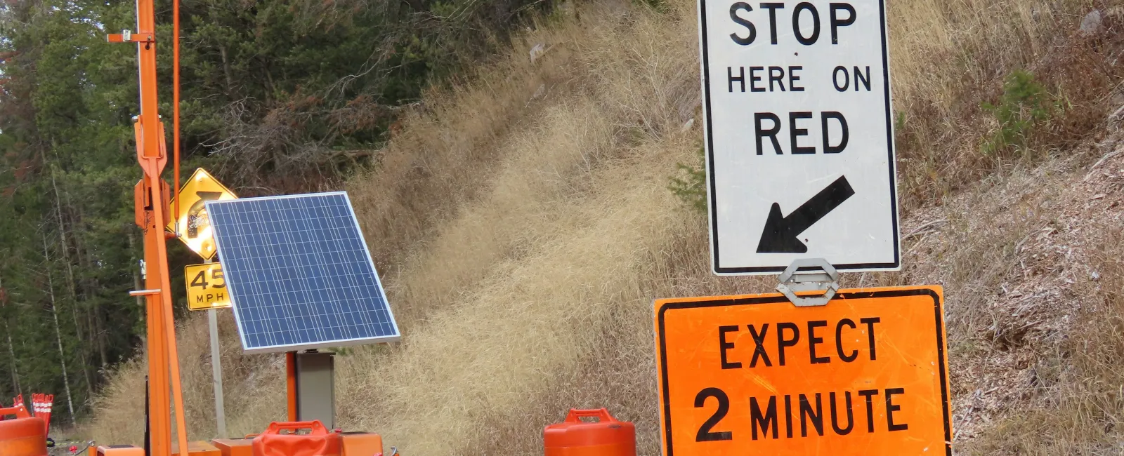 Temporary construction traffic light with signs advising to stop on red and expect 2-minute wait time