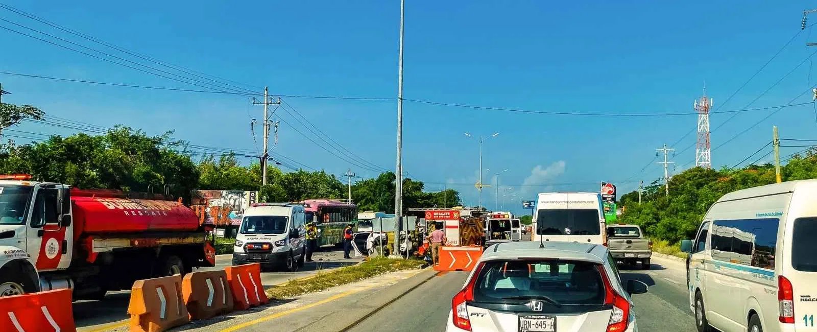 Traffic congestion with multiple vehicles including cars, vans, and a red tanker truck on a sunny day with blue sky.