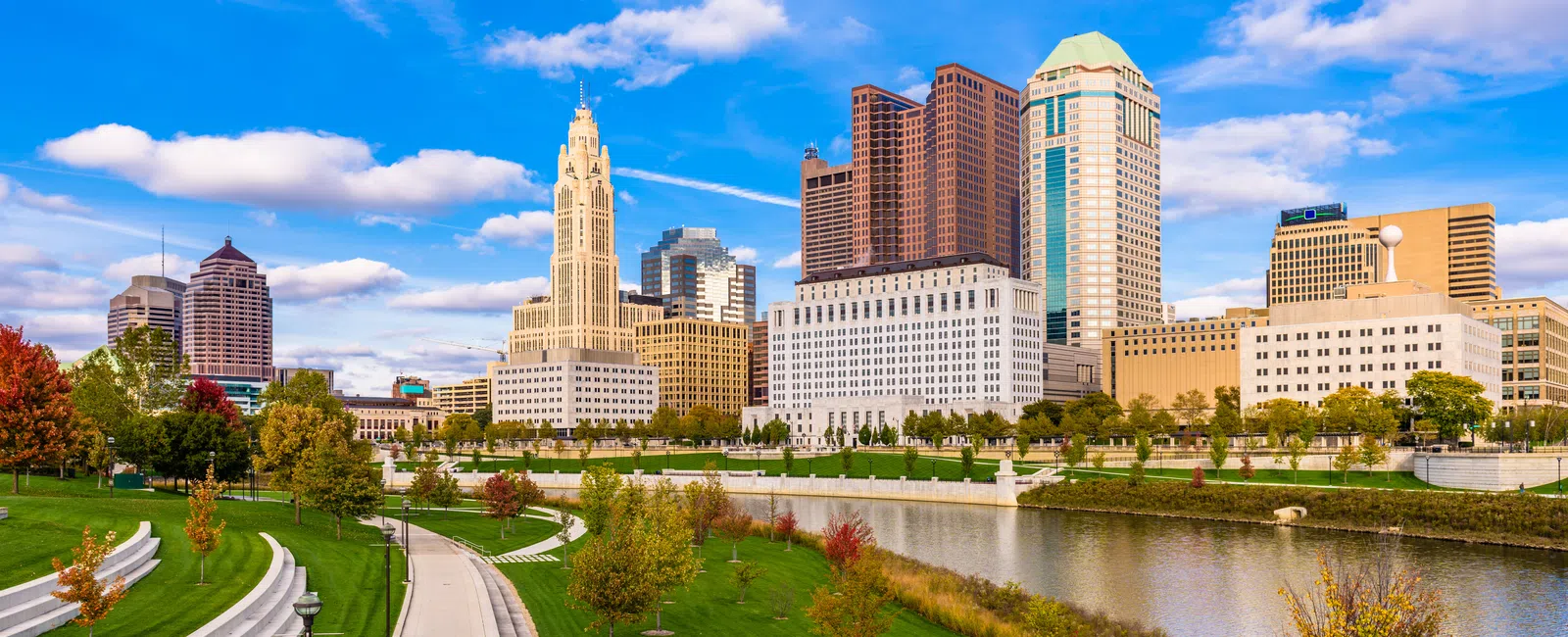 Columbus Ohio skyline with riverfront park and autumn trees under a vibrant blue sky on a sunny day