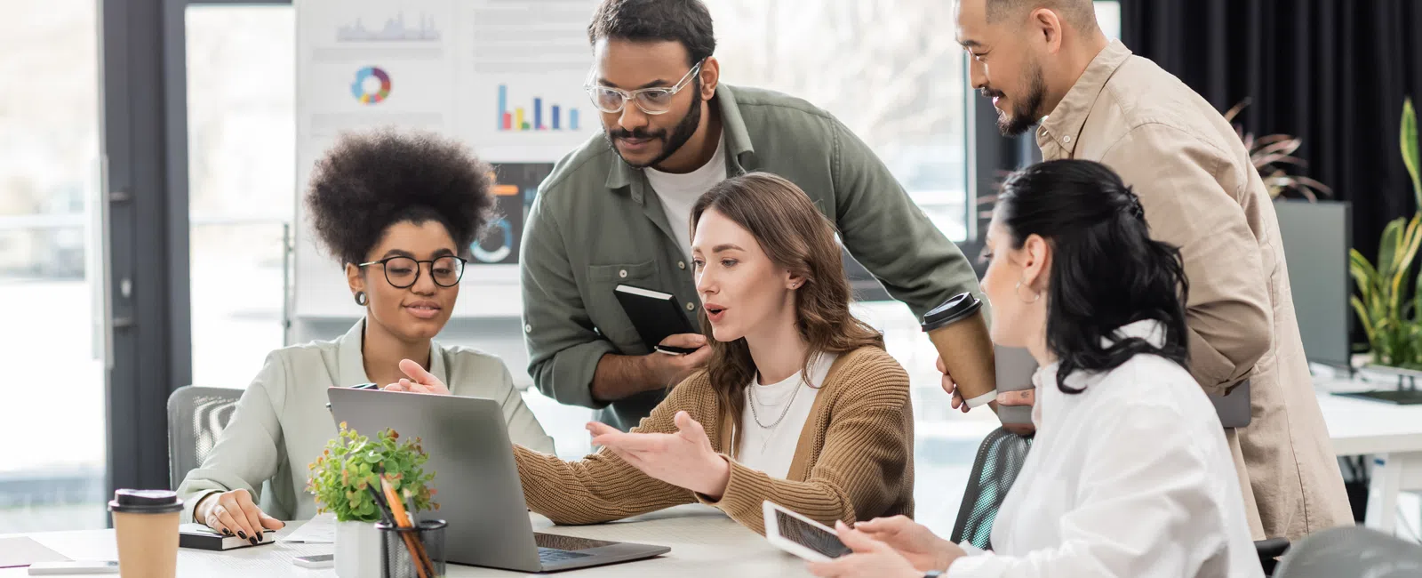 Diverse group of young professionals collaborating on a project using a laptop in a modern office.