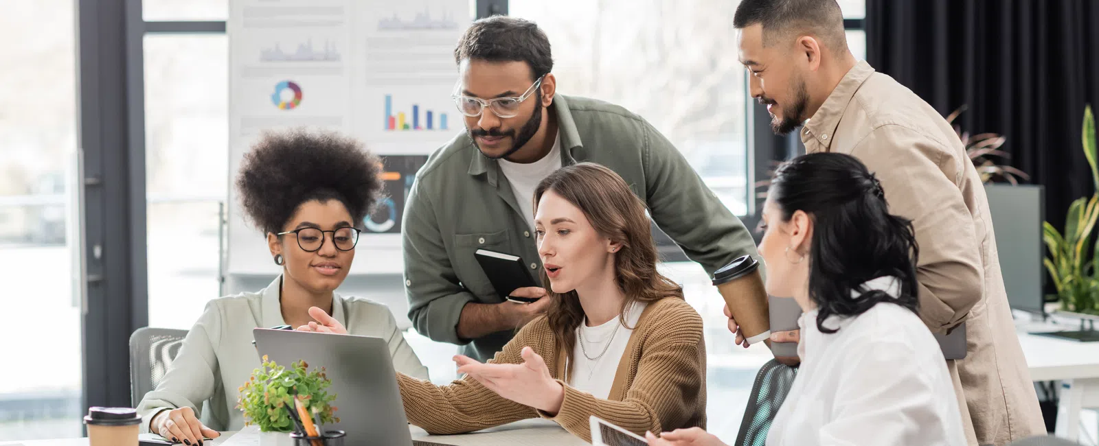 Diverse group of young professionals collaborating on a project using a laptop in a modern office.